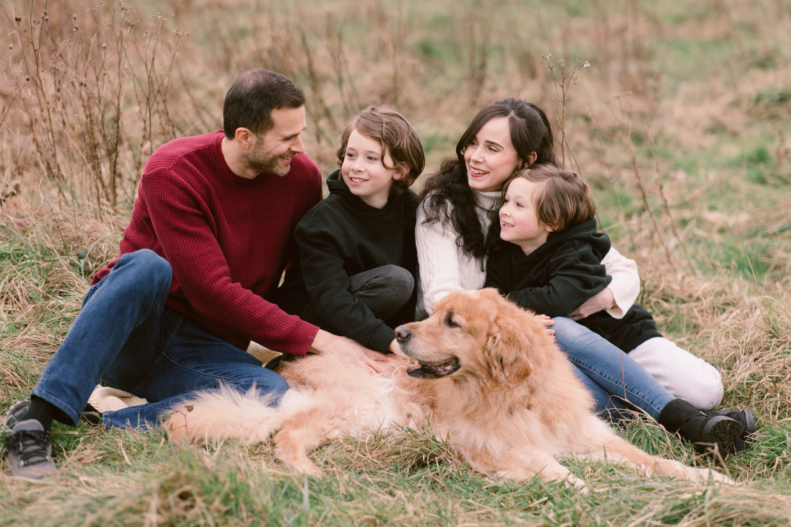 Hampshire Family Photographer with dog Hampshire Family Photographer - Family sat in the grass looking at each other with their golden retriever dog