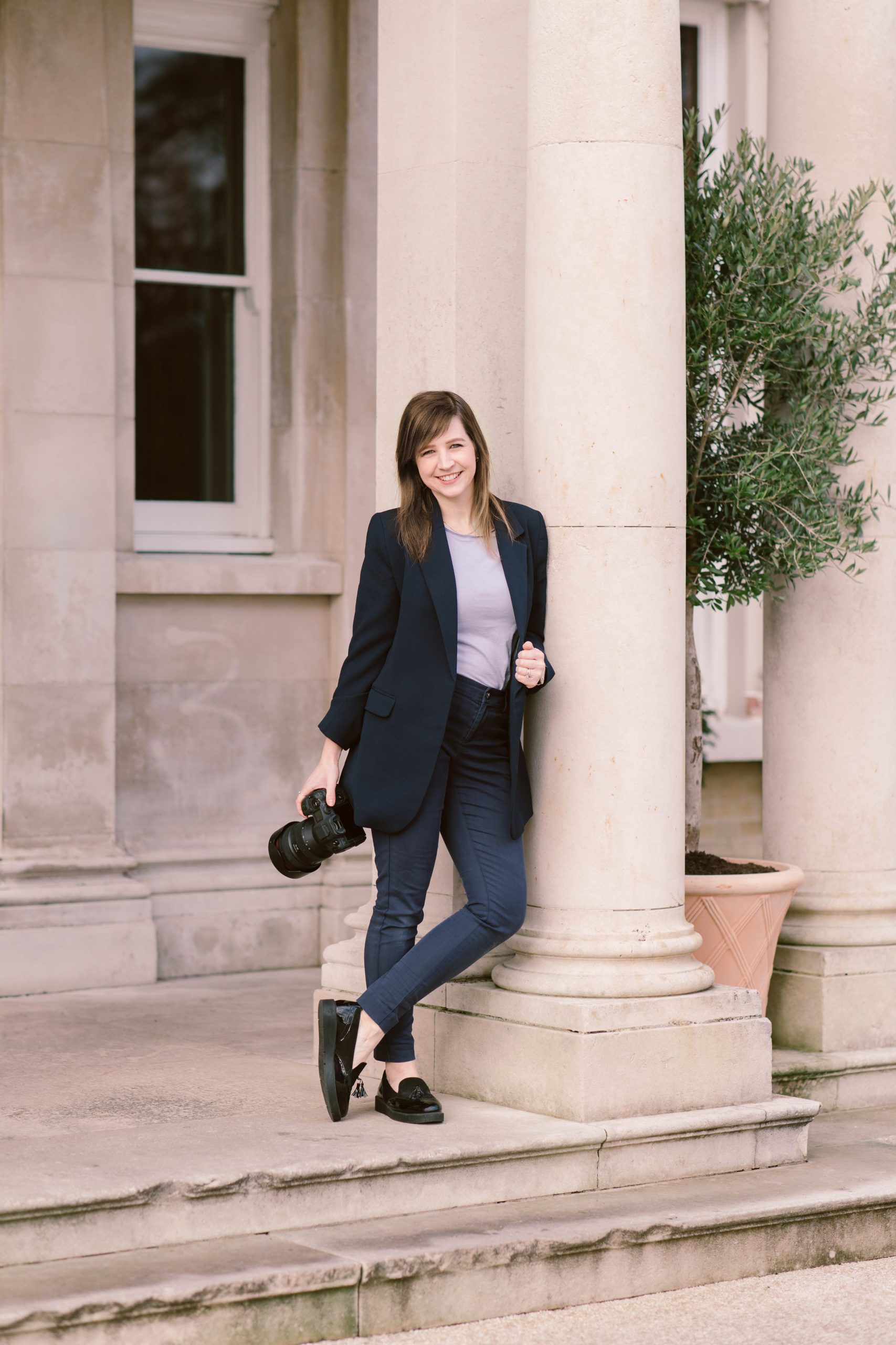 Lucy owner of Lucylou Photography Lucy perched against wall holding camera, owner of Lucylou Photography - Hampshire Wedding Photographer